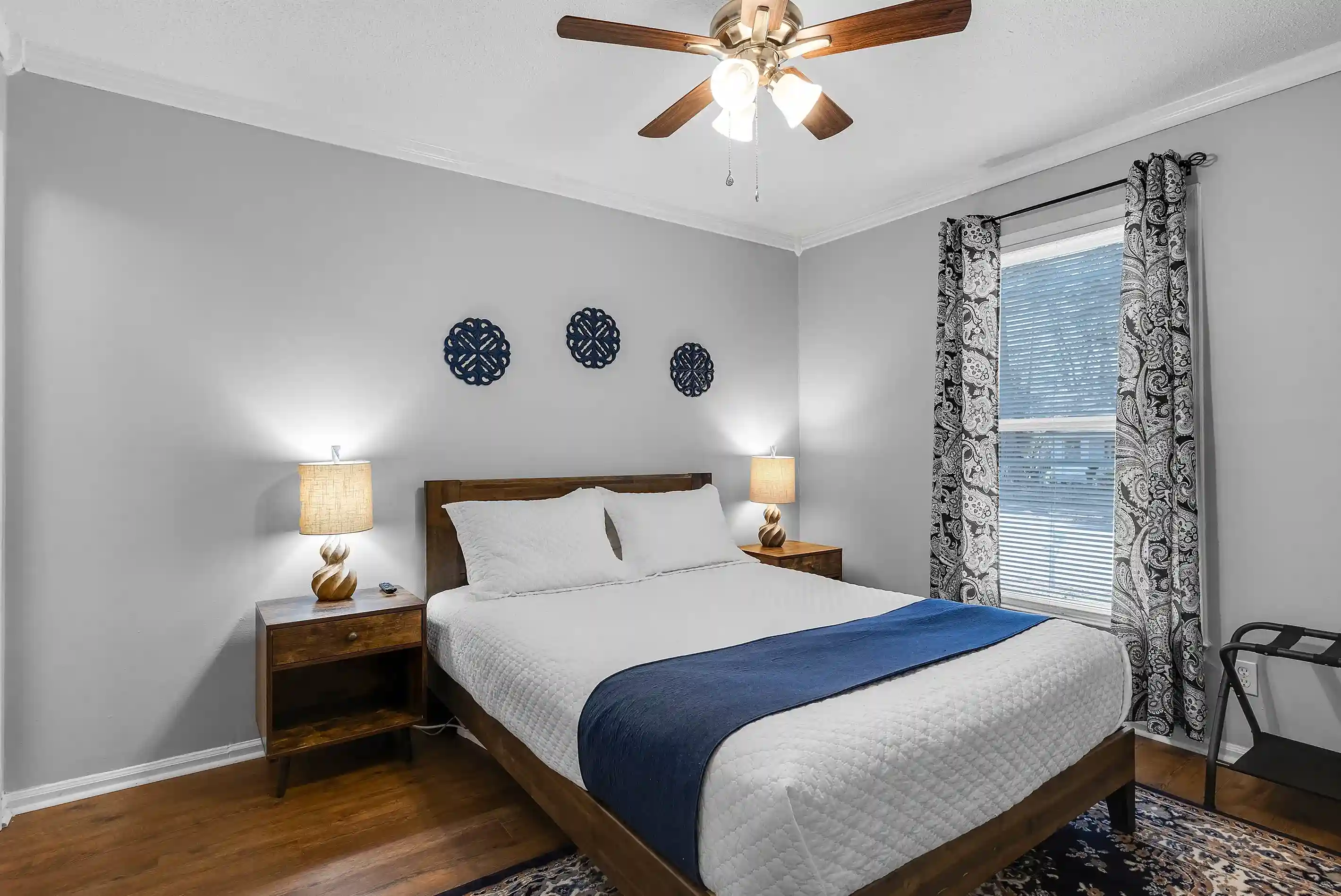 The primary bedroom, with an en-suite bathroom features a queen bed, nightstands with lamps, a luggage rack and a wall- mounted smart TV.